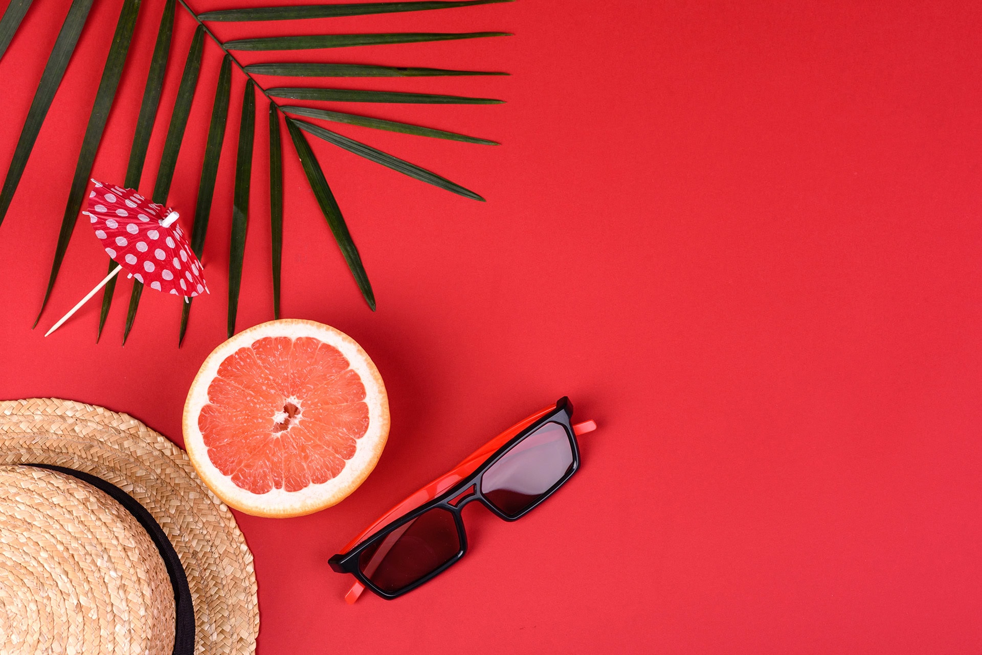Urlaubsschild mit Sonnenbrille, Hut und Grapefruit auf rotem Hintergrund.